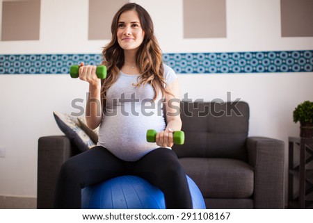 Happy pregnant mom exercising at home with a stability ball and dumbbells