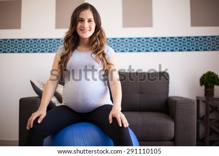 Gorgeous young pregnant mother sitting in a stability ball at home and smiling