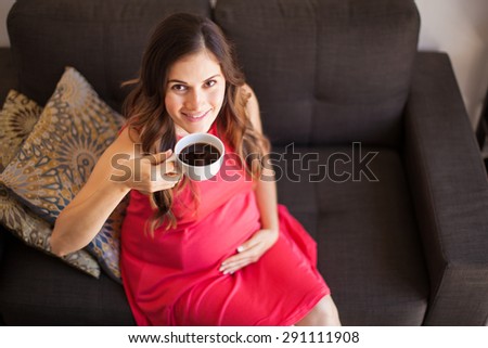 Portrait of a gorgeous young pregnant woman enjoying a cup of coffee at home and smiling