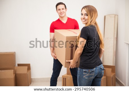 Happy good looking couple carrying a big box and smiling in their new home