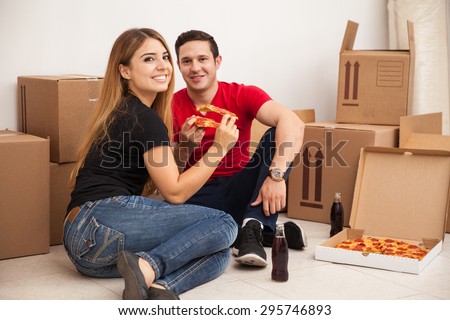 Attractive Hispanic young couple eating pizza while moving into their new apartment