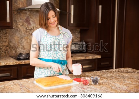 Pretty young woman adding some frosting and fruit to a cake she just baked at home