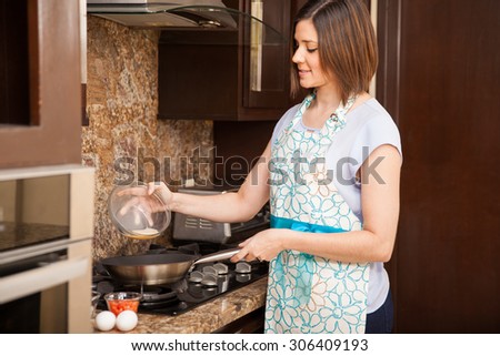 Attractive young woman pouring some eggs in a frying pan at home and making an omelette