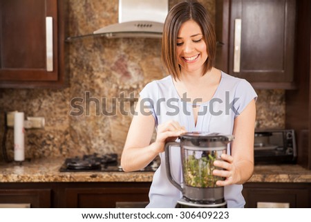 Happy young woman using a blender to make a healthy green juice at home