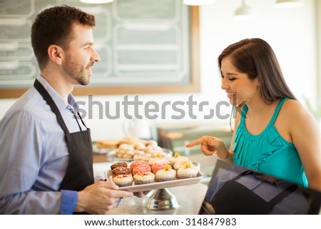 Profile view of a cute female customer pointing at a cupcake she wants to buy in a cake shop. Focus on woman