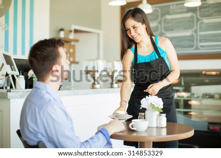 Gorgeous young Latin waitress bringing a cupcake and some coffee to a customer in a cafe