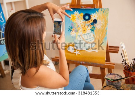 Rear view of a young woman taking a photo of her most recent painting to share it and sell it online