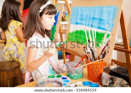 Beautiful little girl taking a moment to look at her painting during art class