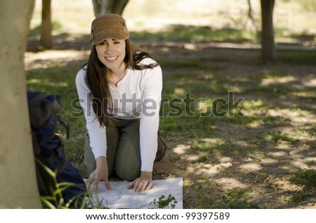 Young brunette looking to a map on the ground and smiling on hiking trip