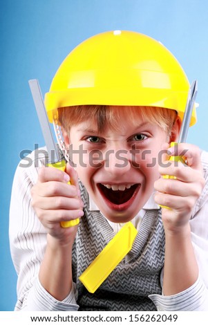 Beautiful cheerful blond boy as a construction worker wearing a yellow hard hat and colorful tools grimacing (job concept)