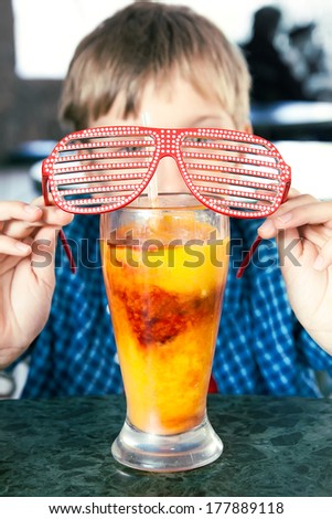Funny child with party sunglasses drinking a fruit cocktail from a big glass. Creative drink concept.
