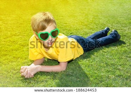 Beautiful happy child with funny sunglasses lying on green grass in a sunny park