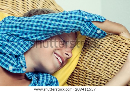 Beautiful funny little child lying on cozy wicker sofa dreaming and laughing. Closeup portrait.