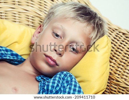 Beautiful funny little child lying on cozy wicker sofa looking sad and sick. Closeup portrait.