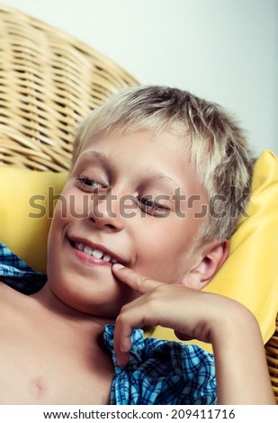 Beautiful funny little child lying on cozy wicker sofa dreaming and smiling. Closeup portrait.