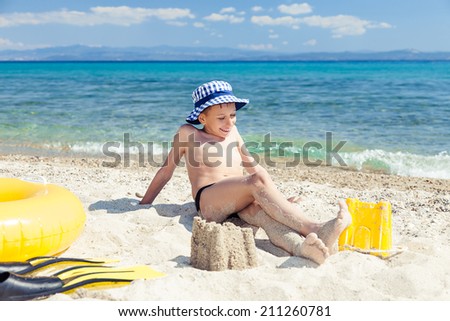 Funny little child with a panama sitting on beach with swimming accessories and relaxing