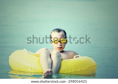 Funny child with swimmer goggles on summer vacation in sea looking displeased and angry. Bad vacation concept.