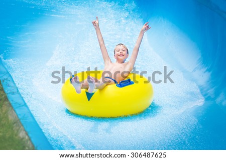 Funny excited child enjoying summer vacation in water park riding yellow float laughing.