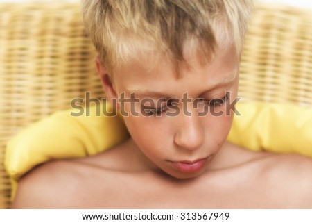 Close up portrait of beautiful funny little child sitting on wicker sofa looking very sad and frustrated. Vintage effect, soft-focus.