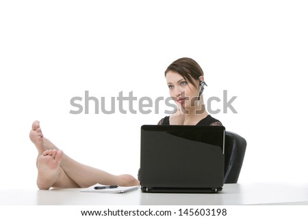 Barefoot young businesswoman relaxing at her desk behind her laptop wearing a headset with a bored expression staring into space