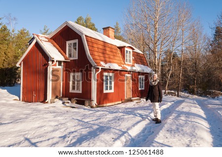 Young woman in winter clothes in front of a characteristic red wooden house in Sweden in a wonderful winter landscape