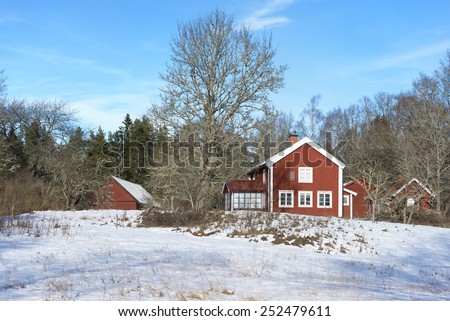 Old red wooden farm house and barns in Sweden under a clear blue sky in winter.