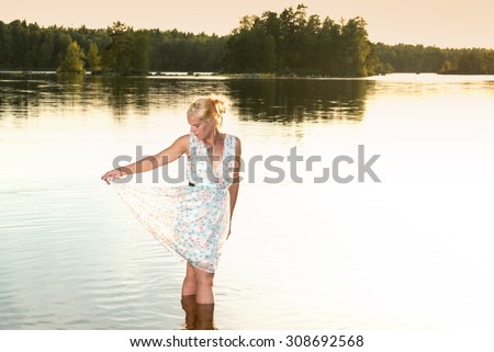 Down by the lake. Young attractive woman in summer dress cools down on a warm summer evening in the lake.