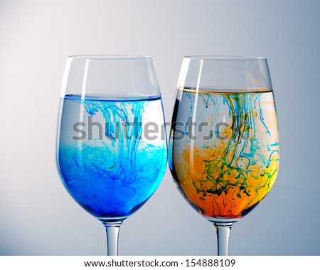 Two wine glasses filled with water and spreading red,yellow  and blue ink