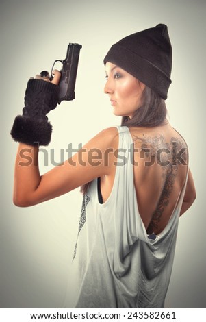 girl with tattoo with a gun standing in the studio