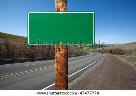 Blank green traffic sign on wooden electric pole against winding road