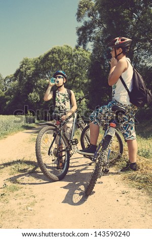 Two teenagers with bicycles relaxing on a bike trip in sunny day, retro colors