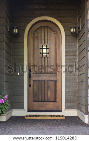 Elegant front door of an upscale home. Front view of an elegant front door on a dark wooden home with porch lights in view. Vertical shot.