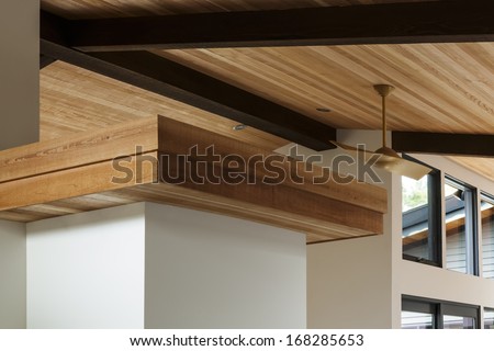 Detail of sloped wood beam ceiling  with modern ceiling fan in a mid-century house. Also seen are windows.