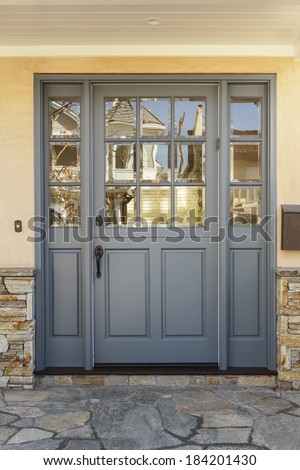 A gray front door to a family home with windows, and shale porch detail. Also seen is doorbell and mailbox.