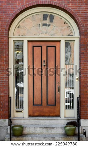 Black Panel Wood Door in Brick Building with Large Lunette Overhead and Decorative Pots on Steps