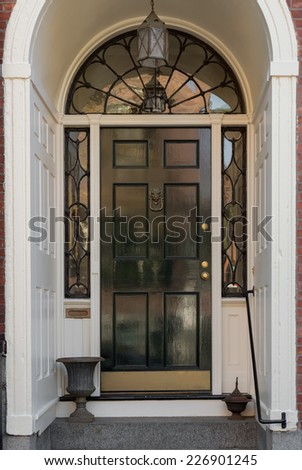 Ornate Entryway with Shiny Black Front Door, Overhead Lunette, and Hanging Lamp in White Archway