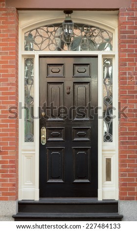 Black Front Door and Surrounding White Door Frame with Ornate Windows in Brick Building