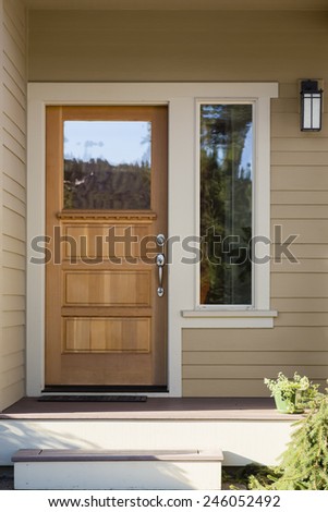 Natural Wood Front Door with Surrounding White Door Frame, Tan Siding, and Windows