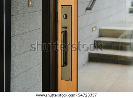 A brass door handle with turning lock knob and thumb latch. A small set of steps are reflected in the glass. Horizontal shot.