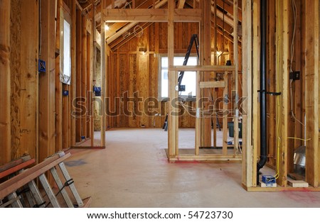 An interior view of a new home under construction with exposed wiring and and a ladder on the floor. Horizontal shot.