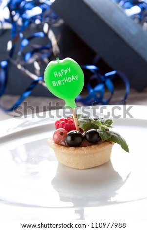 Happy birthday candle in the form of a green lollipop stuck into a small individual fresh fruit tartlet with a crisp pastry base