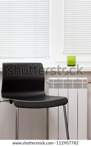 Empty modern black modular chair with tubual metal legs in a white minimalist house interior alongside a radiator