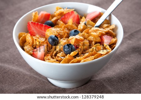 Bowl of healthy corn flakes breakfast cereal topped with fresh blackcurrants and strawberries served in a white ceramic bowl for a delicious meal
