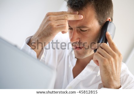 Stressed businessman with headache at the office talking on phone