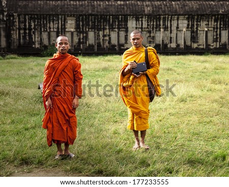 ANGKOR WAT, CAMBODIA - NOVEMBER 8, 2013: Two monks in orange and yellow robes pose in one of the inner courtyards of Angkor Wat in Cambodia on November 8, 2013. On is holding a tablet computer.