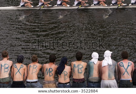 A group of young men rooting and cheering and providing encouragement to their rowing club during a crew race on Opening Day in Seattle. Their backs are painted with the name of their club.