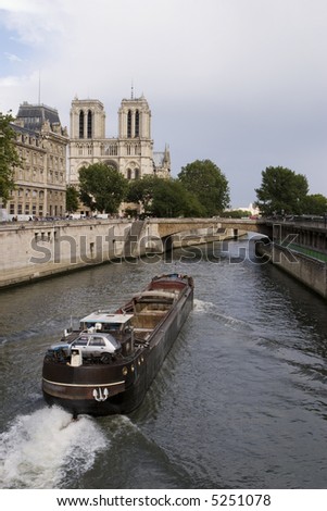 A French river boat moving downstream on the Seine River in the narrow river channel near Notre Dame and the Ile de France.