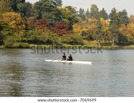 Pair Rowing In Autumn. A racing shell with two people warming up prior to a race; background is colorful autumn leaves.