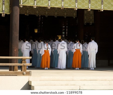 A group of priests are lined up into five rows of five people each, receding into the shadow of the inner sanctuary of the temple. This was viewed at a traditional Shinto temple in Japan.