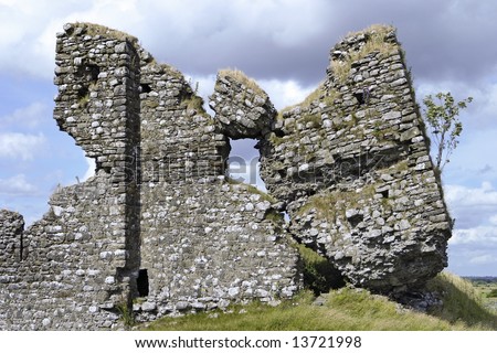 The ruined facade of Clonmacnoise Castle in County Offaly, Ireland. The ruins show elements of the old stone walls tilting on a little knoll or hill in the country.